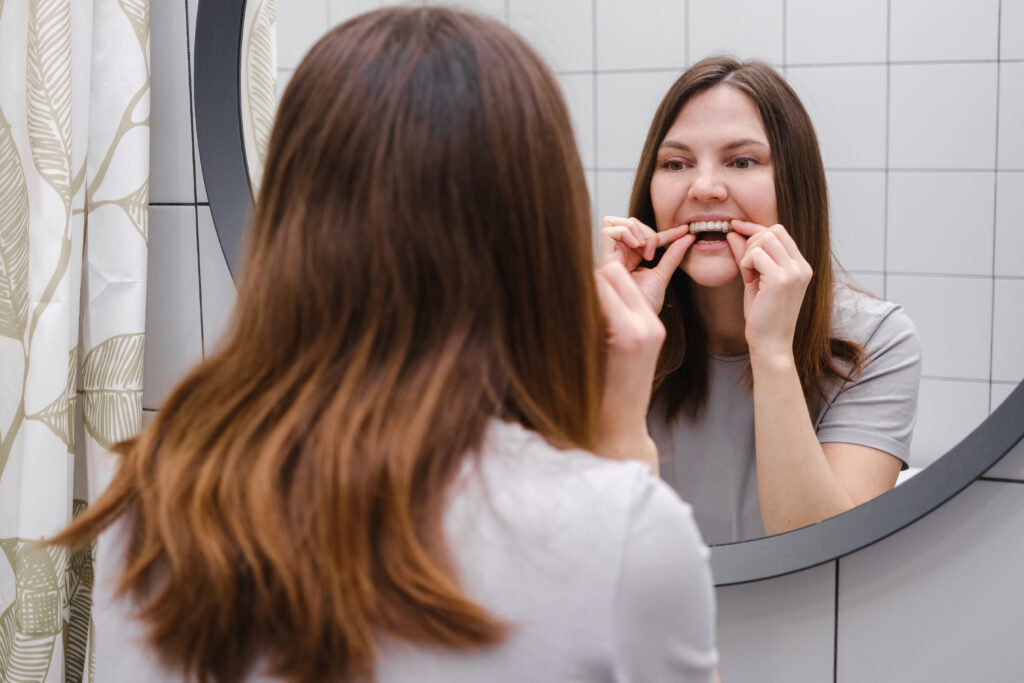 a woman in front of a mirror in the bathroom holding invisible plastic teeth aligners in hands and putting on braces. beautiful and healthy smile.