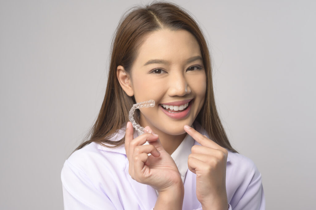 young female dentist holding invisalign braces over white background studio, dental healthcare and orthodontic concept.