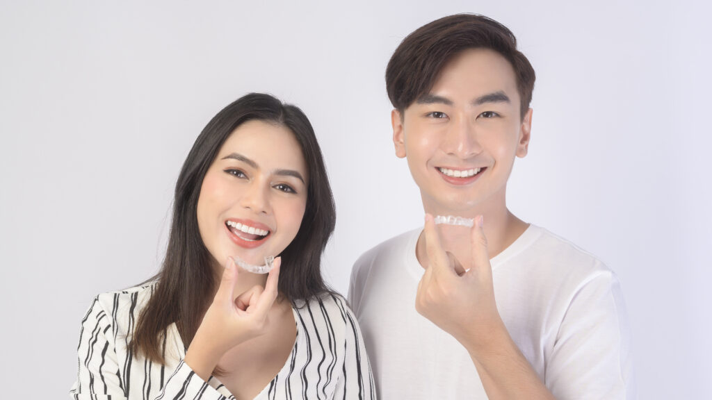 young smiling man amd woman holding invisalign braces over white background studio, dental healthcare and orthodontic concept.
