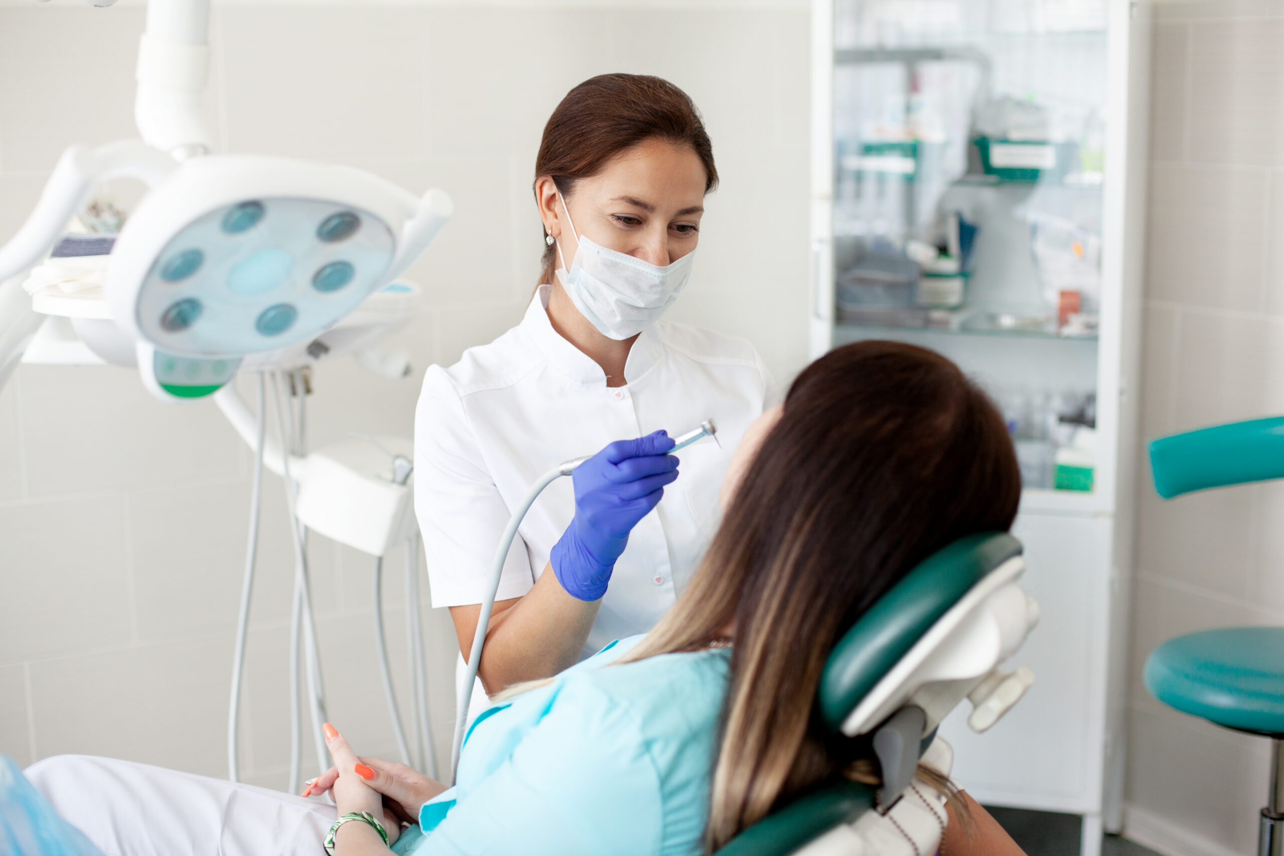 woman dentist treats a patient. a woman in a mask sits in a dental chair in the clinic.