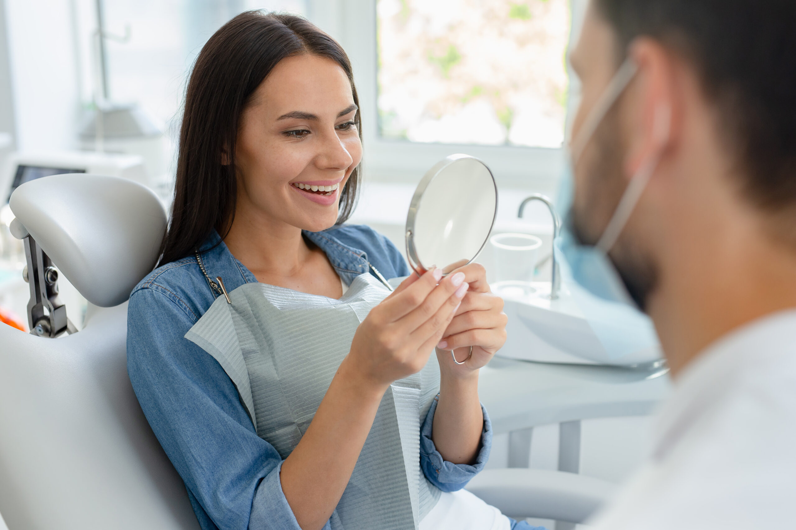 selective focus of young woman looking in mirror after dental procedure